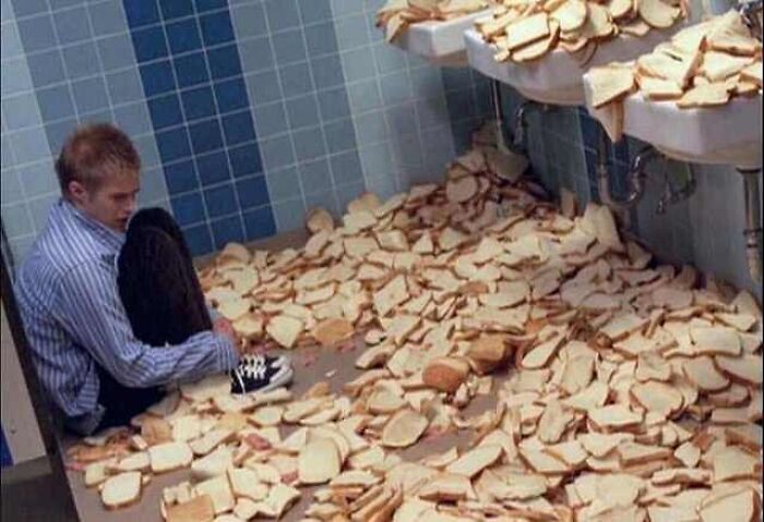 Young man sitting on the floor of a bathroom filled with slices of bread, creating a cursed image moment.