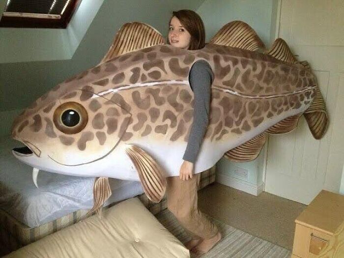 Woman holding a giant fish costume indoors, a cursed image perfect for a weird brain break moment.