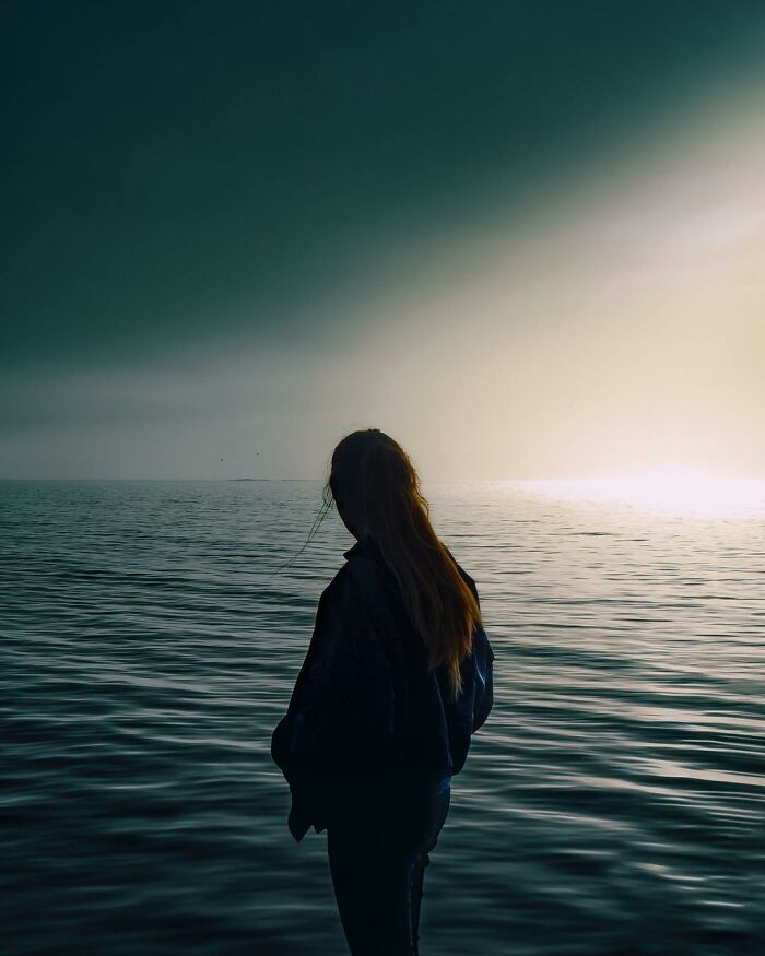 Silhouette of a woman looking at the ocean horizon at sunset, a creative photo manipulation evoking surreal reality.
