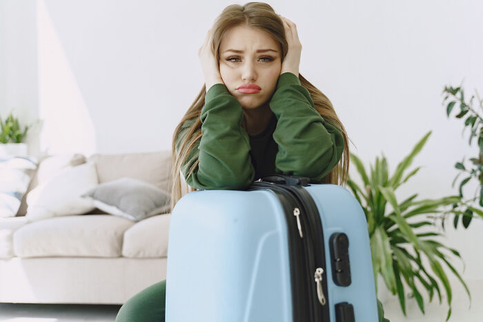 Sad young woman leaning on a suitcase indoors, showing how a tiny thing made the trip better despite travel troubles.