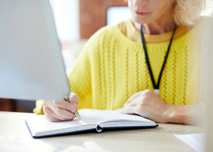 Woman in a yellow sweater writing notes at a desk, illustrating infuriating things said by people in charge.