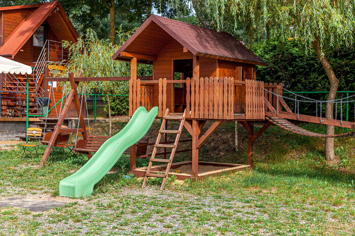 Wooden playground set with green slide and rope bridge surrounded by trees, illustrating wildest life blunders concept.