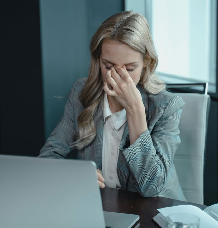 Woman in a business suit showing frustration while working on a laptop, illustrating infuriating things said by people in charge.