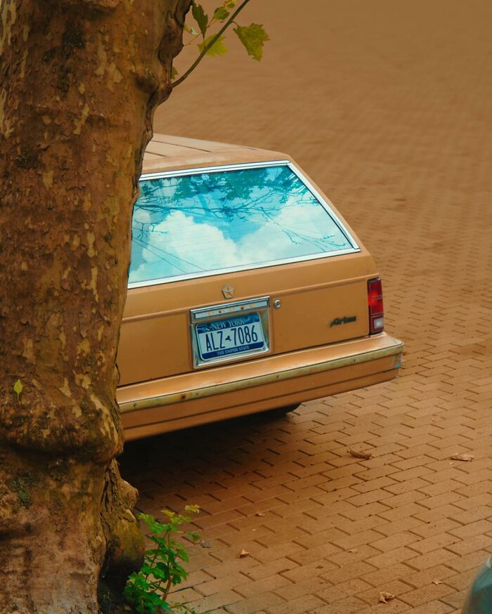 Vintage car with a reflective rear window showing a surreal sky, showcasing creative photo manipulations art.