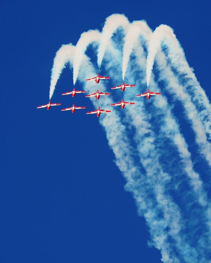 Red airplanes performing aerial stunts with smoke trails against a clear blue sky, showcasing creative photo manipulations.