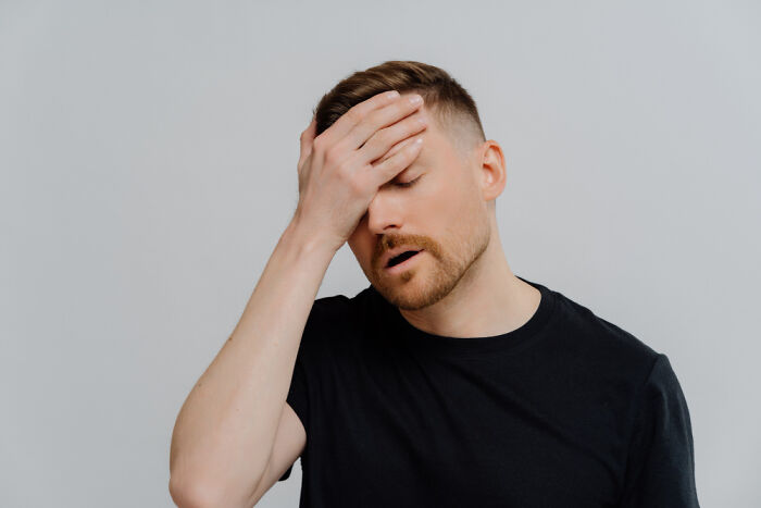 Man in black shirt with hand on forehead expressing frustration or disbelief while thinking about celebrity gossip.