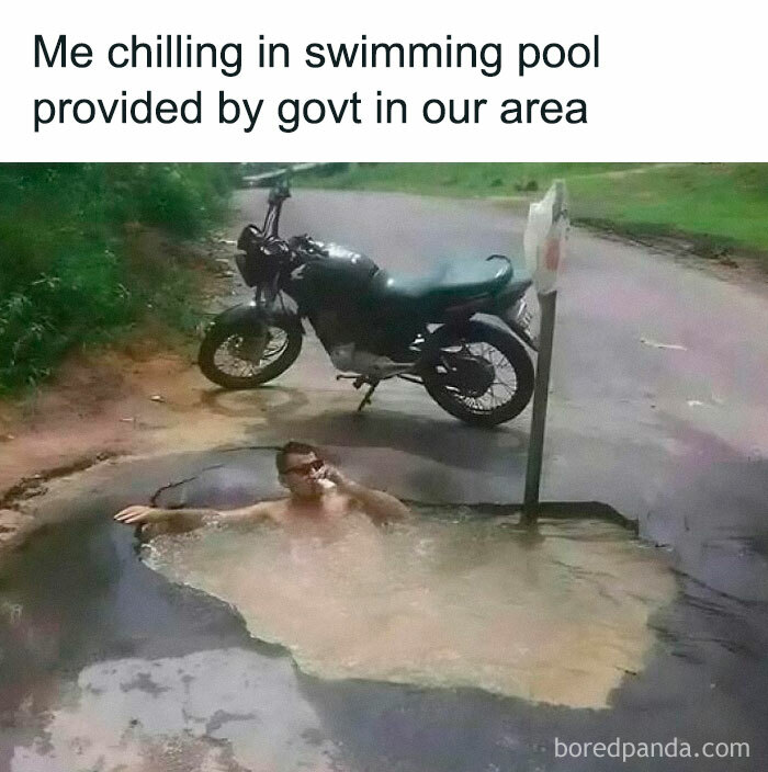 Man relaxing in a muddy water pothole on the road with a motorcycle nearby, hilarious memes content.