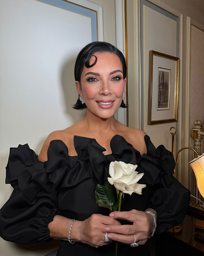 Woman in an elegant black dress holding a white rose, styled with vintage hair and delicate jewelry in a classic room setting. Woman in an elegant black dress holding a white rose, styled with vintage hair and delicate jewelry in a classic room setting.