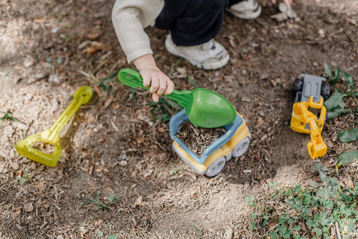 Child playing with toys, digging in dirt and causing damage to neighbor lawn with green shovel and plastic truck. Child playing with toys, digging in dirt and causing damage to neighbor lawn with green shovel and plastic truck.