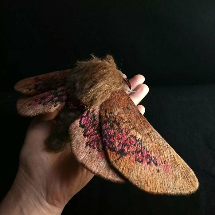 Hand holding a large embroidered fiber moth with detailed brown and pink wings, showcasing beautiful textile art.