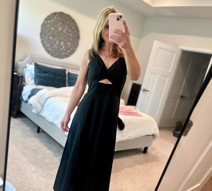 Woman wearing a sleeveless black dress taking a mirror selfie in a bedroom, showcasing warm weather finds for the season.
