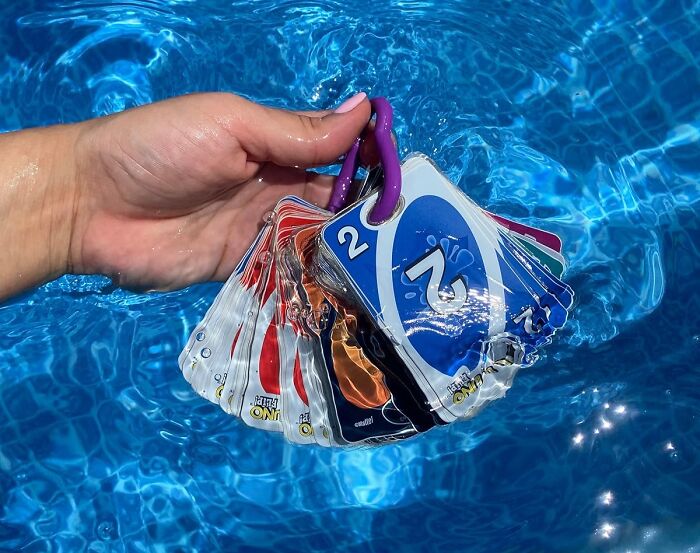 Hand holding waterproof cards fanned out in a pool, showcasing warm weather finds for outdoor fun and relaxation.
