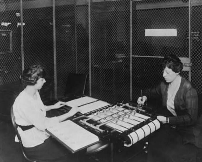 Two women using early computing or tabulating machines in America 100 years ago, showcasing life in the past.