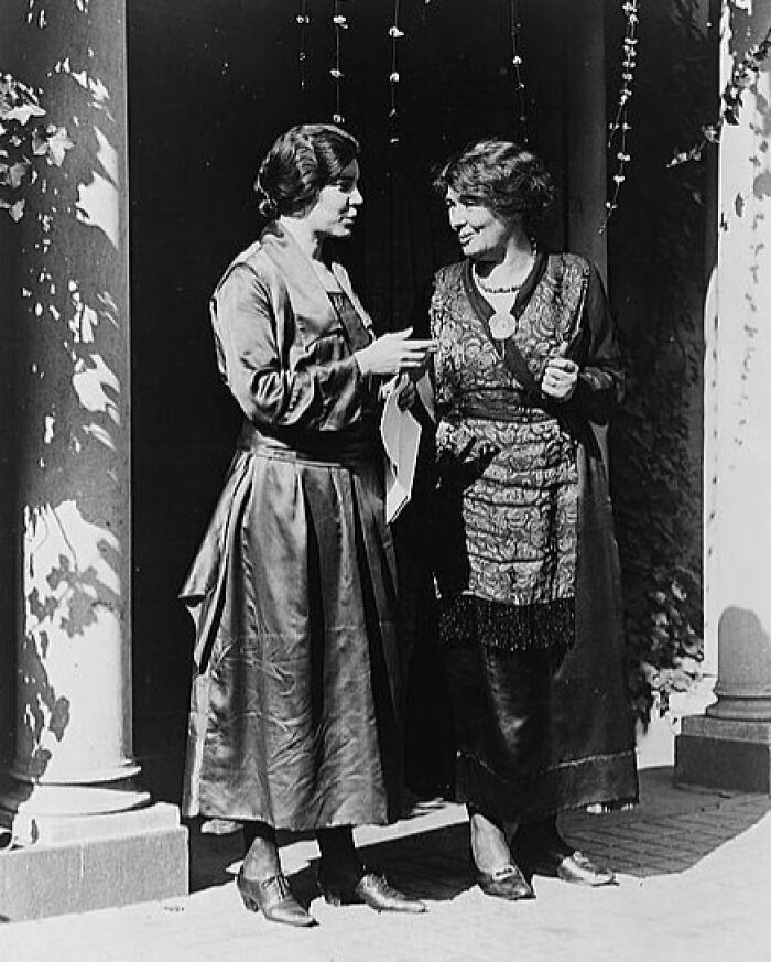 Two women dressed in early 20th century fashion sharing a conversation, showcasing life in America from 100 years ago.