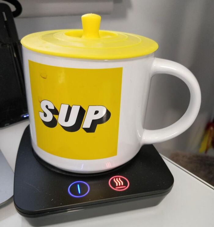 White mug with yellow lid and SUP text on a desk cup warmer, one of the office supplies to improve desk experience.