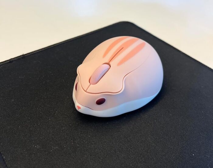 Cute rabbit-shaped computer mouse placed on a black mouse pad as an office supply for a desk setup.