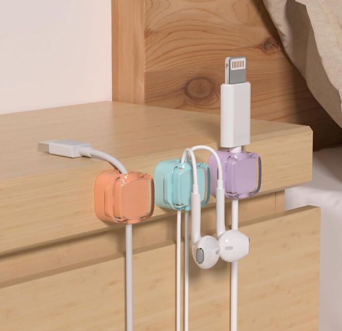 Colorful office supplies cable organizers holding charging and earphone cords on a wooden desk edge for neat workspace.