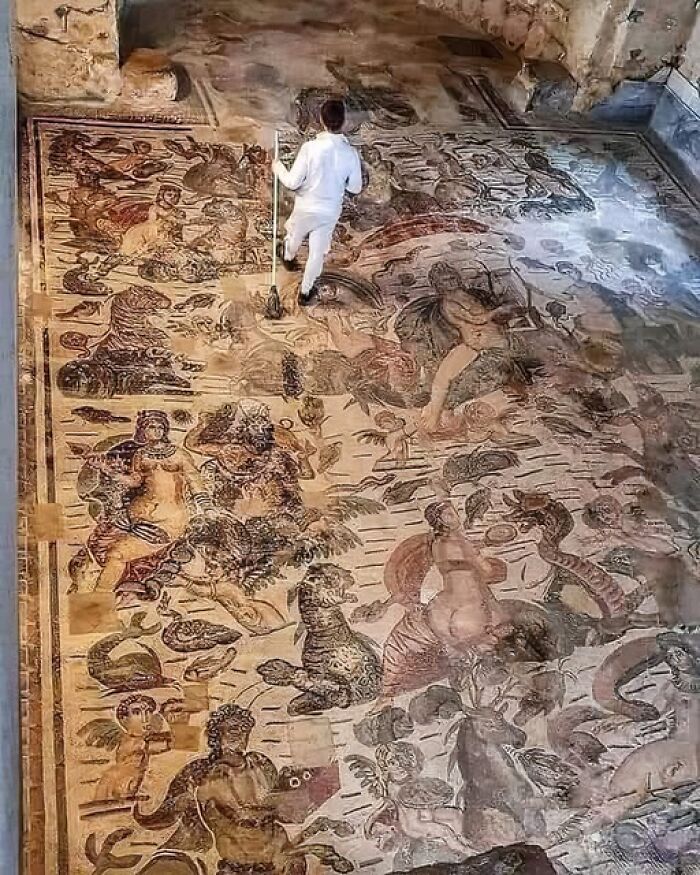 Person cleaning an ancient detailed floor mosaic in an archaeology news and architecture site.