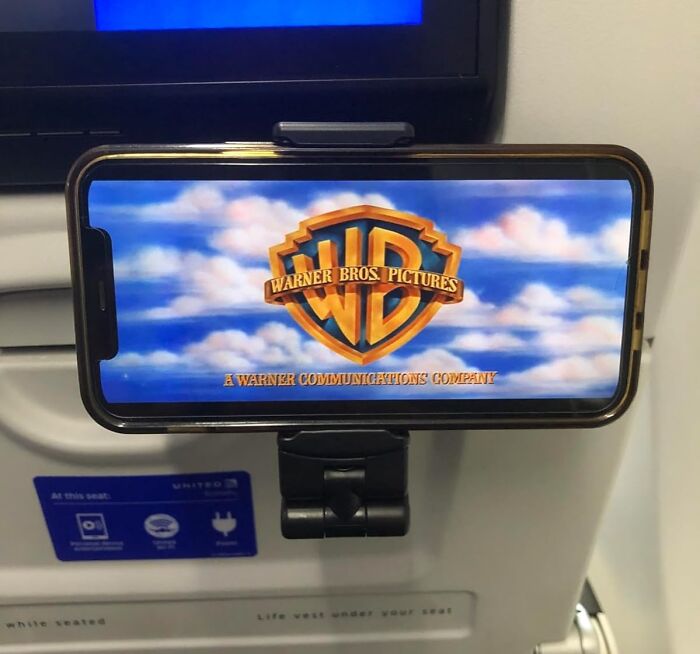 Smartphone mounted on airplane seat showing Warner Bros Pictures logo, a practical find for people who want to nail adulting.