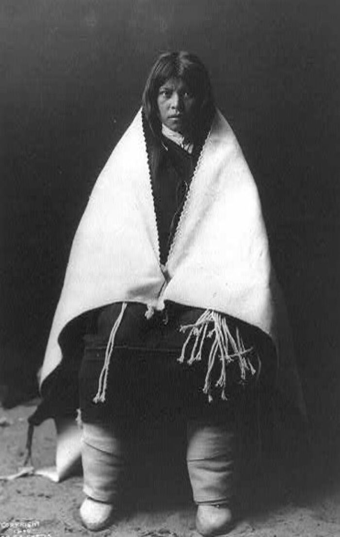 Native American woman wrapped in a traditional blanket, seated, capturing a rare and powerful moment of life in the 1900s.