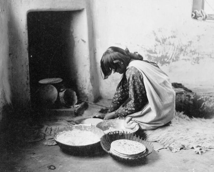Native American woman in the 1900s preparing traditional food inside a rustic home, showcasing early Native American life.