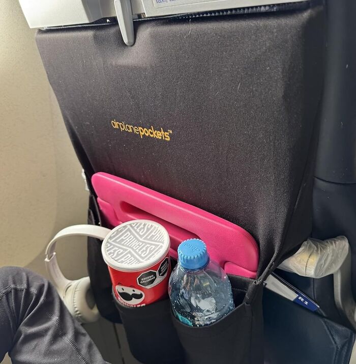 Airplane organizer holding snacks, water, headphones, and a tablet, showcasing in-flight essentials for a first-class feeling.