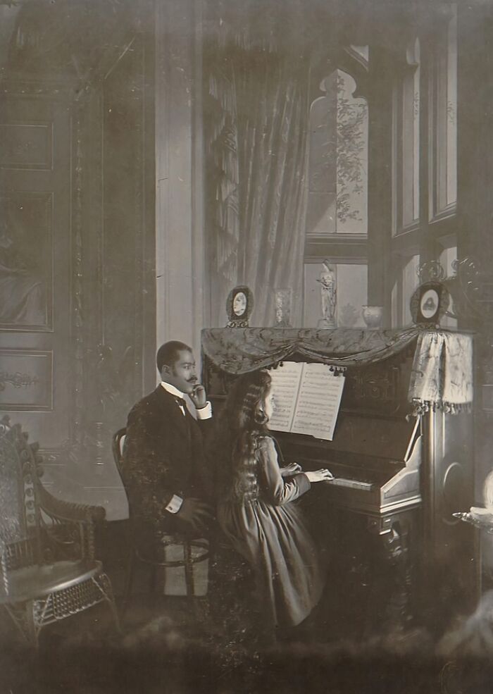 African American man watching young girl play piano in an elegant room, capturing African American life in 1900 Paris.