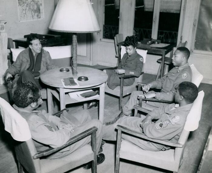 African Americans in uniform sitting and conversing around a table in a historical military setting.