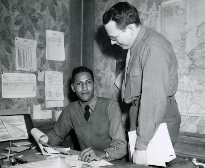 African American man in uniform working at a desk with a colleague in a historical military office setting.