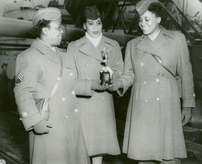 Three African American women in military uniform smiling and holding a trophy, showcasing historic moments in uniform.