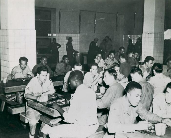 African American and white soldiers in uniform eating together in a historic military canteen during wartime.