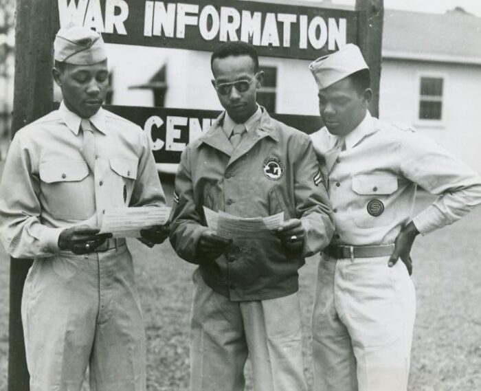 Three African Americans in military uniform reading documents outside a war information center during history.