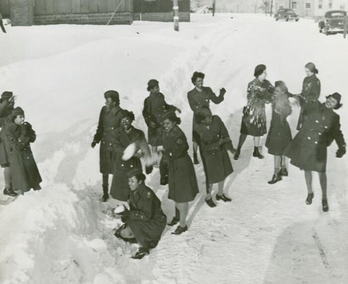 African American women in uniform having a snowball fight outside during winter, showcasing historical moments in uniform.