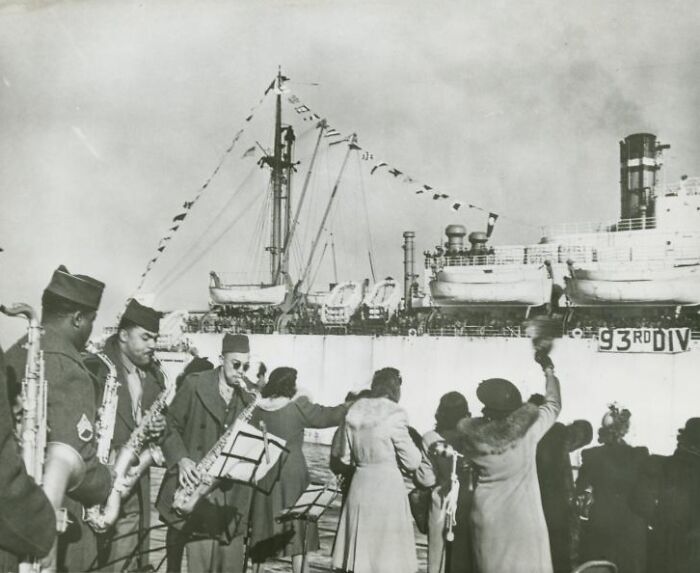 African American military band playing near a docked ship, capturing history of African Americans in uniform.