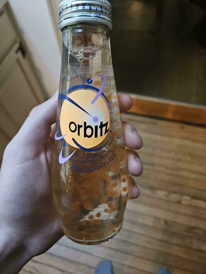 Hand holding a vintage Orbitz drink bottle containing floating orbs, a bizarre thing found in old houses collection.