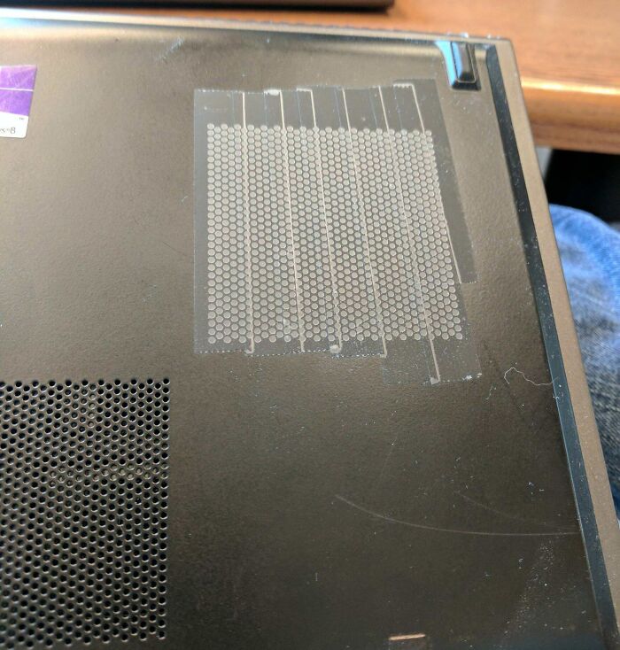 Laptop bottom with damaged ventilation holes covered by poorly placed transparent tape showing technology disasters.