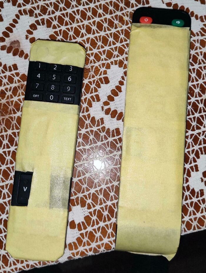 Two TV remote controls wrapped in yellow tape on a patterned tablecloth showing a tech disaster fail example.