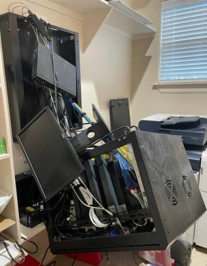 Network equipment and monitors collapsed on the floor, illustrating technology disasters and engineering failures in a small office room.