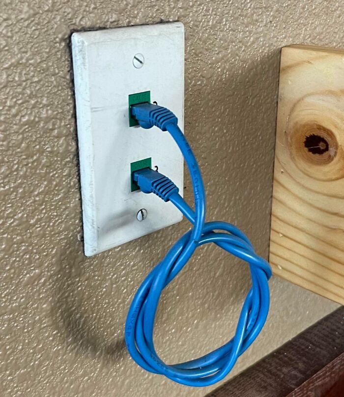 Blue Ethernet cable looped back into the same wall port, illustrating a technology disaster caused by improper network connection.