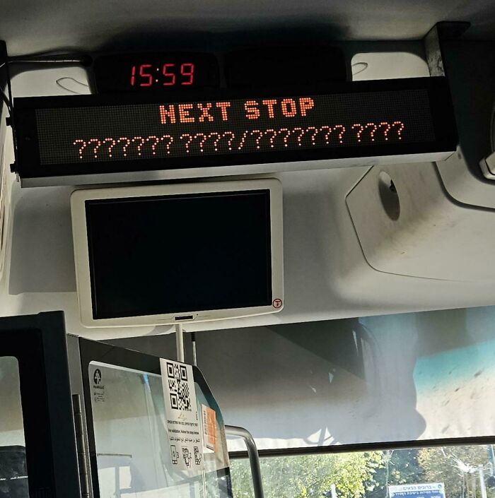 Bus interior showing a digital display with a technology disaster error displaying unreadable characters for the next stop.