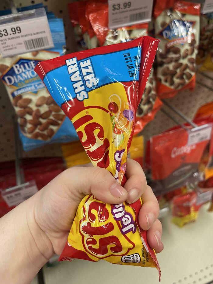 Hand squeezing a small, share-size bag of Skittles in a store, illustrating products getting smaller and more expensive.