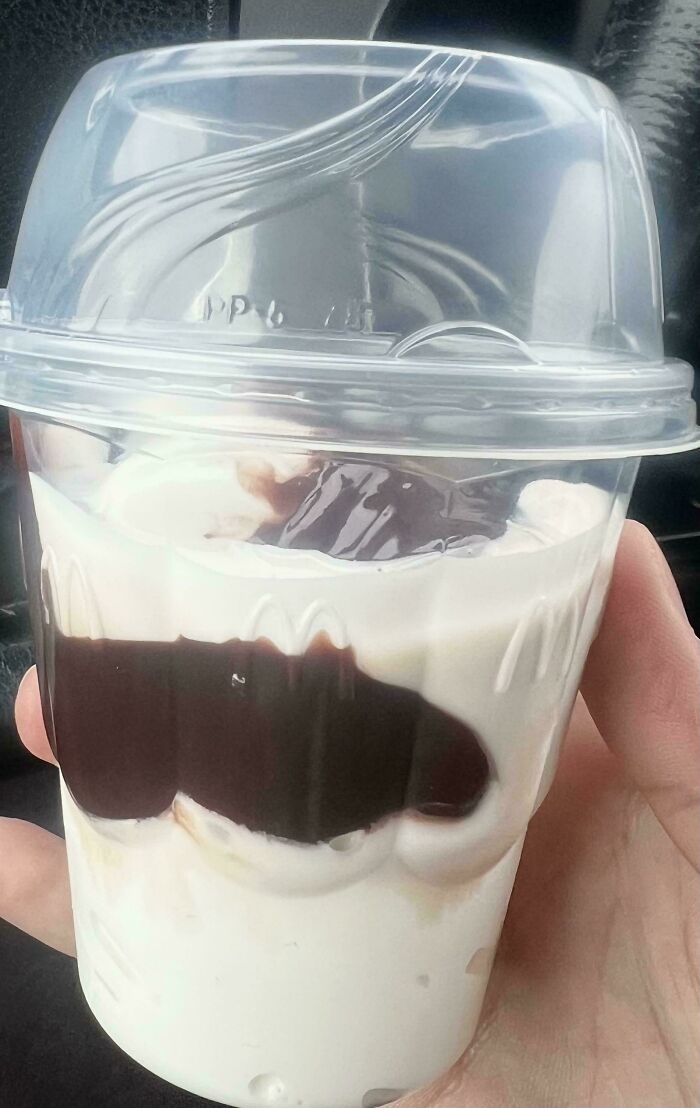 Hand holding a small, partially melted ice cream sundae with chocolate syrup, showing smaller products and packaging.