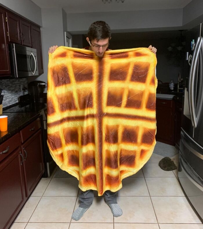 Person in kitchen holding a waffle blanket, one of the hilarious finds under $10 for affordable fun and laughter.