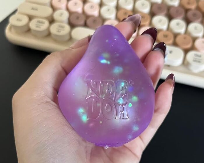 Hand holding purple Nee Doh stress ball with colorful specks, a funny find under $10 for laughter and stress relief.