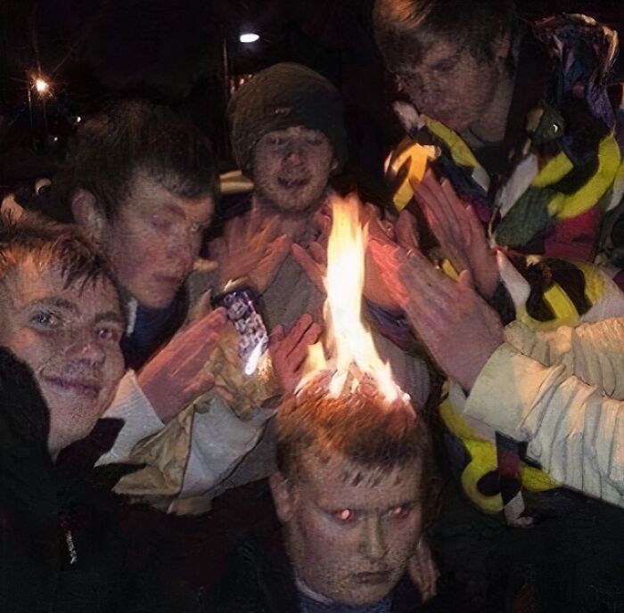 Group of teenagers with one person appearing to have a cursed image effect of fire on their head at night outdoors.