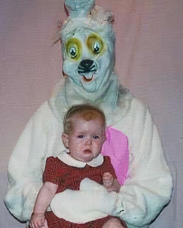 Cursed image of a baby sitting with a person in a creepy, worn animal costume with distorted facial features.