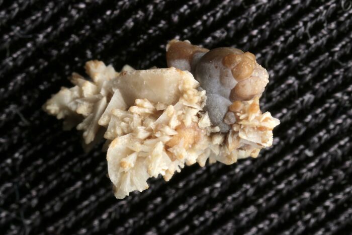 Close-up photo of a bizarre human body kidney stone with crystallized formations on a dark textured fabric background Close-up photo of a bizarre human body kidney stone with crystallized formations on a dark textured fabric background