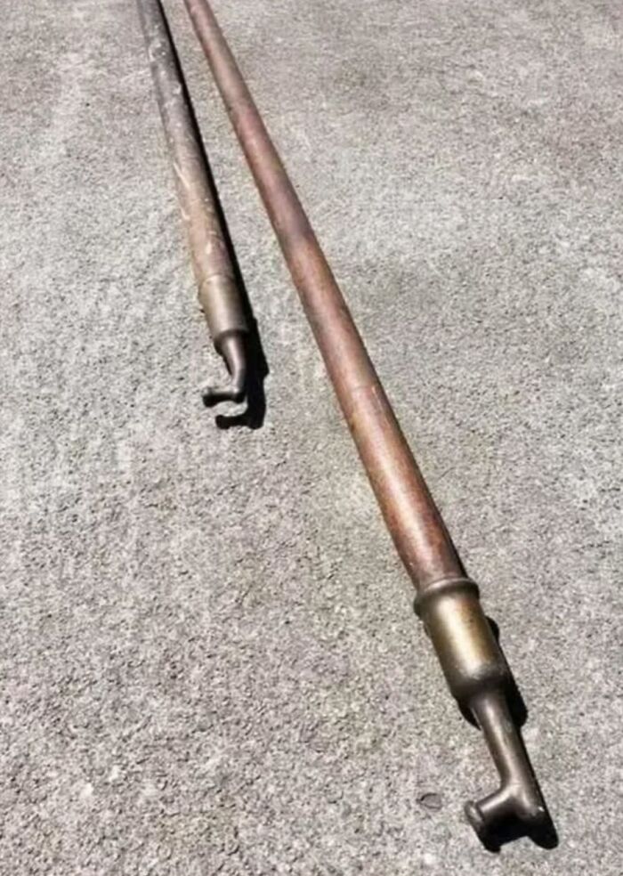 Two long rusty metal pipes with hooked ends lying on a rough concrete surface, strange things found in homes. Two long rusty metal pipes with hooked ends lying on a rough concrete surface, strange things found in homes.