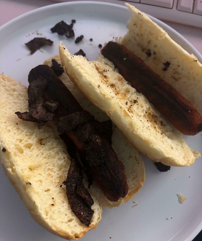 Burnt hot dogs in buns on a white plate showing a cooking fail and accident in the kitchen.