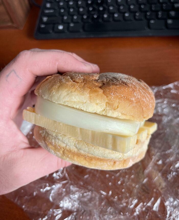 Hand holding a sandwich with thick slices of raw onion and cheese, showcasing a cooking fail and accident.